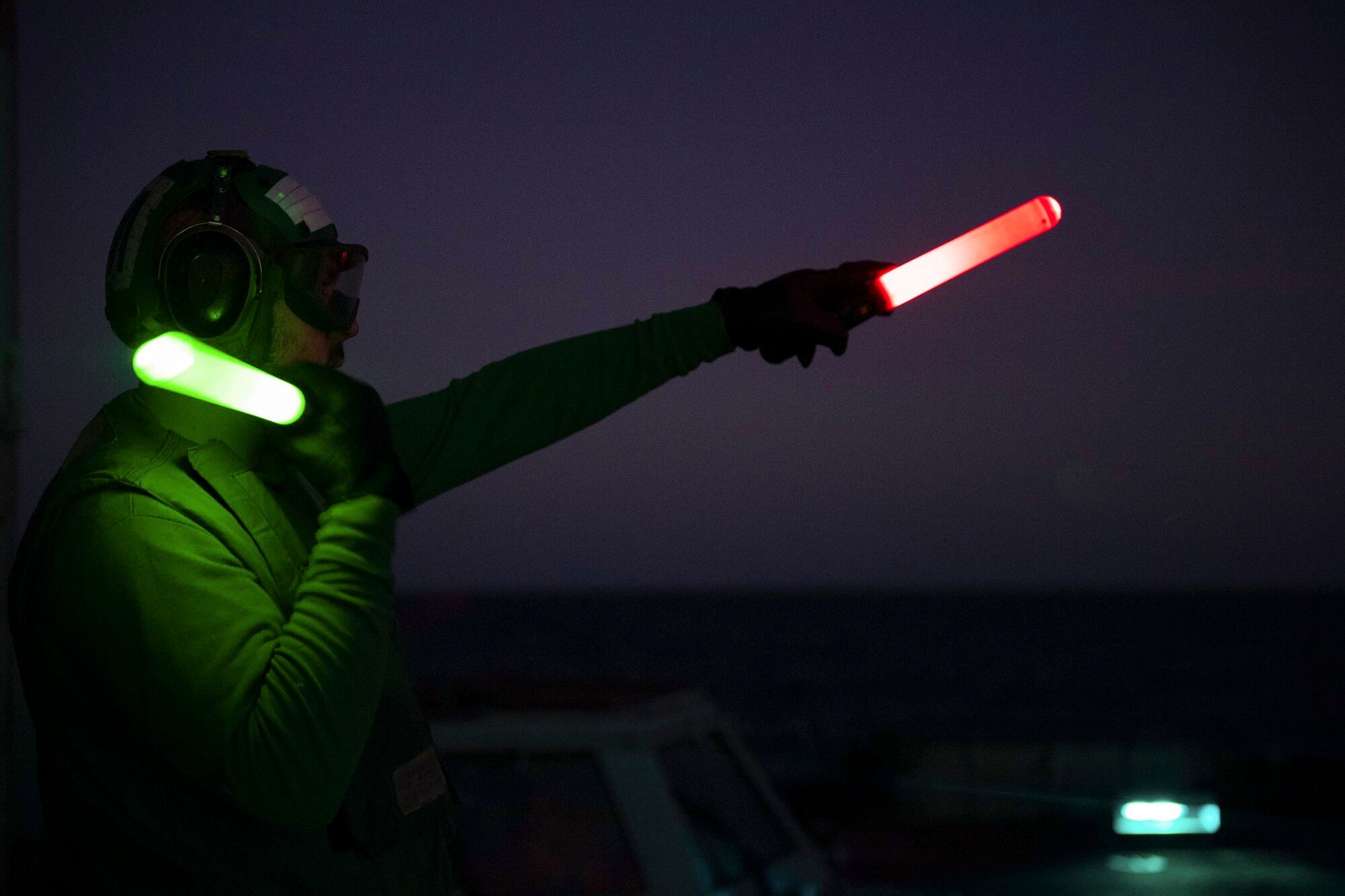 Aviation Maintenance Administrationman Robert Murdolo signals to the pilots of an MH-60R Sea Hawk helicopter Dec. 15, 2020, during night flight operations aboard the guided-missile cruiser USS Princeton (CG 59) in the North Arabian Sea.