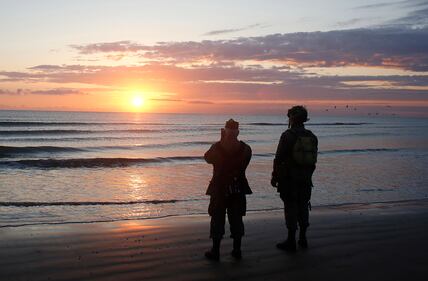 World War II re-enactors stand looking out to sea on Omaha Beach in Normandy, France