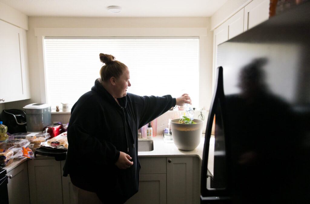 Heather Nguyen waters her plant with bottled water in her home on the Joint Base Lewis-McChord base, May 8, 2023.