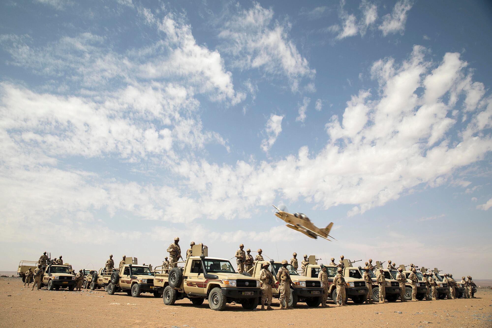 An A-29B Super Tucano flies over Mauritanian Army soldiers as they pose for a picture in Atar, Mauritania, Feb. 17, 2020, during Flintlock 2020, U.S. Africa Command's largest annual special operations forces exercise.