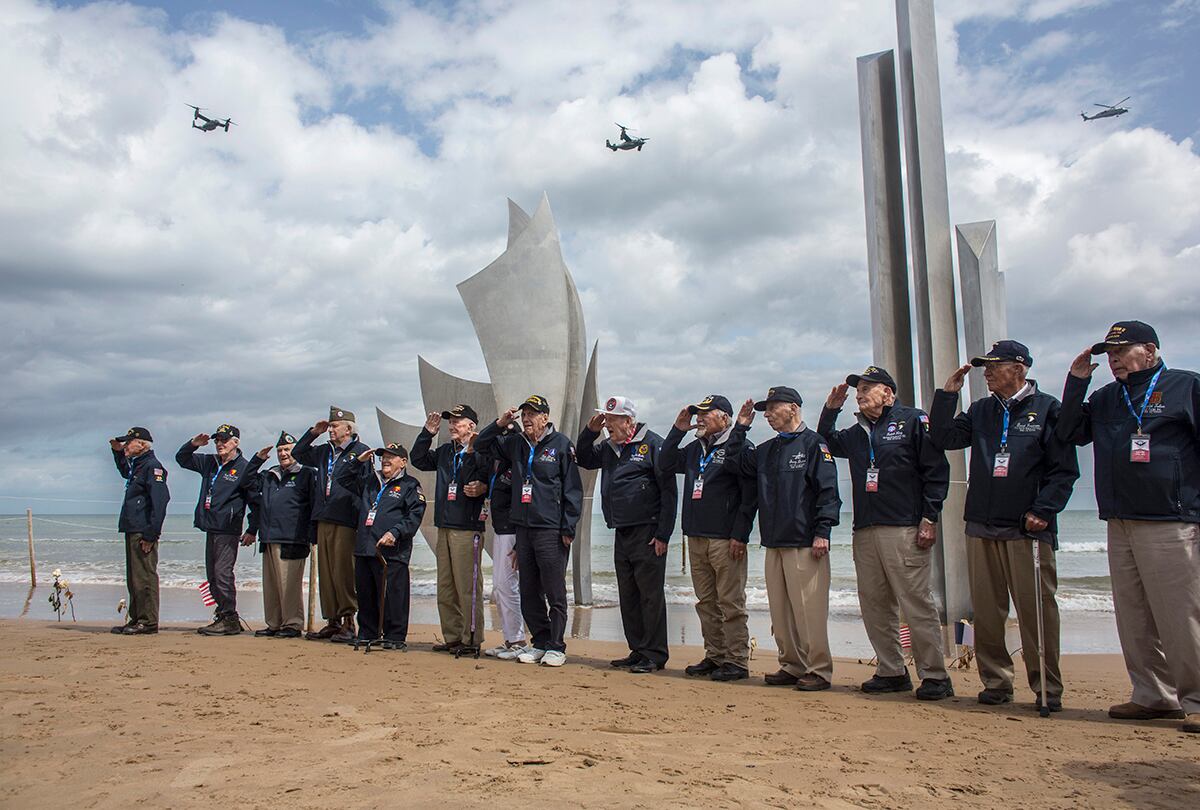 World War II veterans from the United States salute as they pose in front of Les Braves monument at Omaha Beach in Saint-Laurent-sur-Mer, Normandy, France