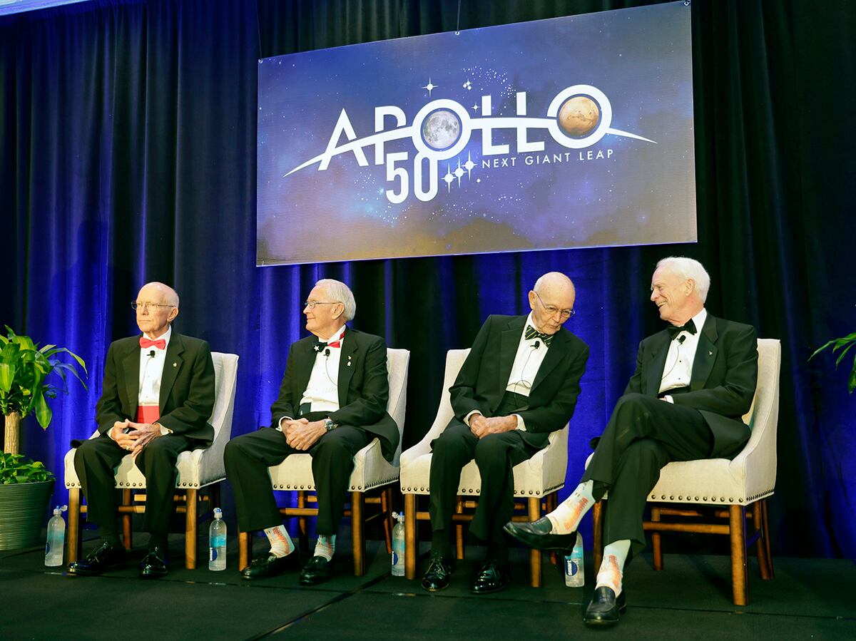 Apollo Legends attend a news conference from left, Gerry Griffin, Apollo flight director, and Charlie Duke, Apollo 16 astronaut, take their seats as Mike Collins, Apollo 11 astronaut admires Apollo 9 astronaut Rusty Schweickart's socks featuring a Saturn V rocket, during a news conference Tuesday, July 16, 2019, in Cocoa Beach, Fla.