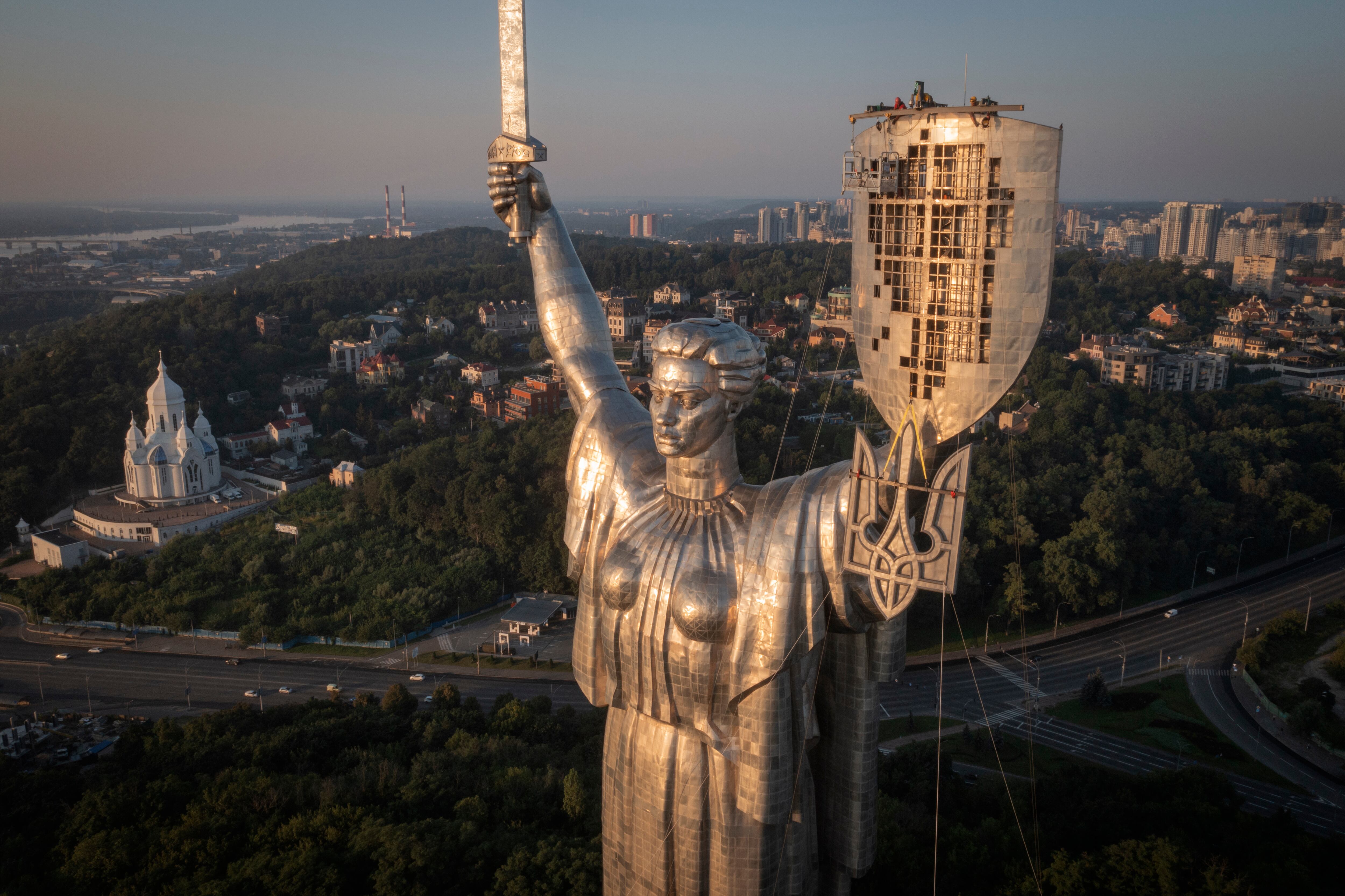 Workers install the Ukrainian coat of arms on the shield in the hand of the country's tallest stature, the Motherland Monument, after the Soviet coat of arms was removed, in Kyiv, Ukraine, Sunday, Aug. 6, 2023.