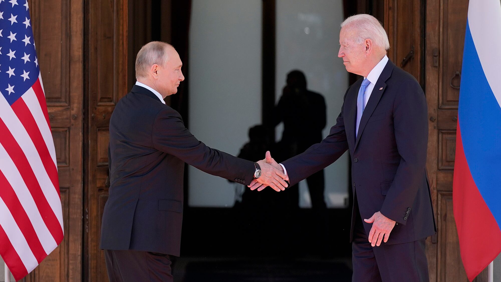 Russian President Vladimir Putin, left, shakes hands with U.S. President Joe Biden in front of the Russian and American flags.