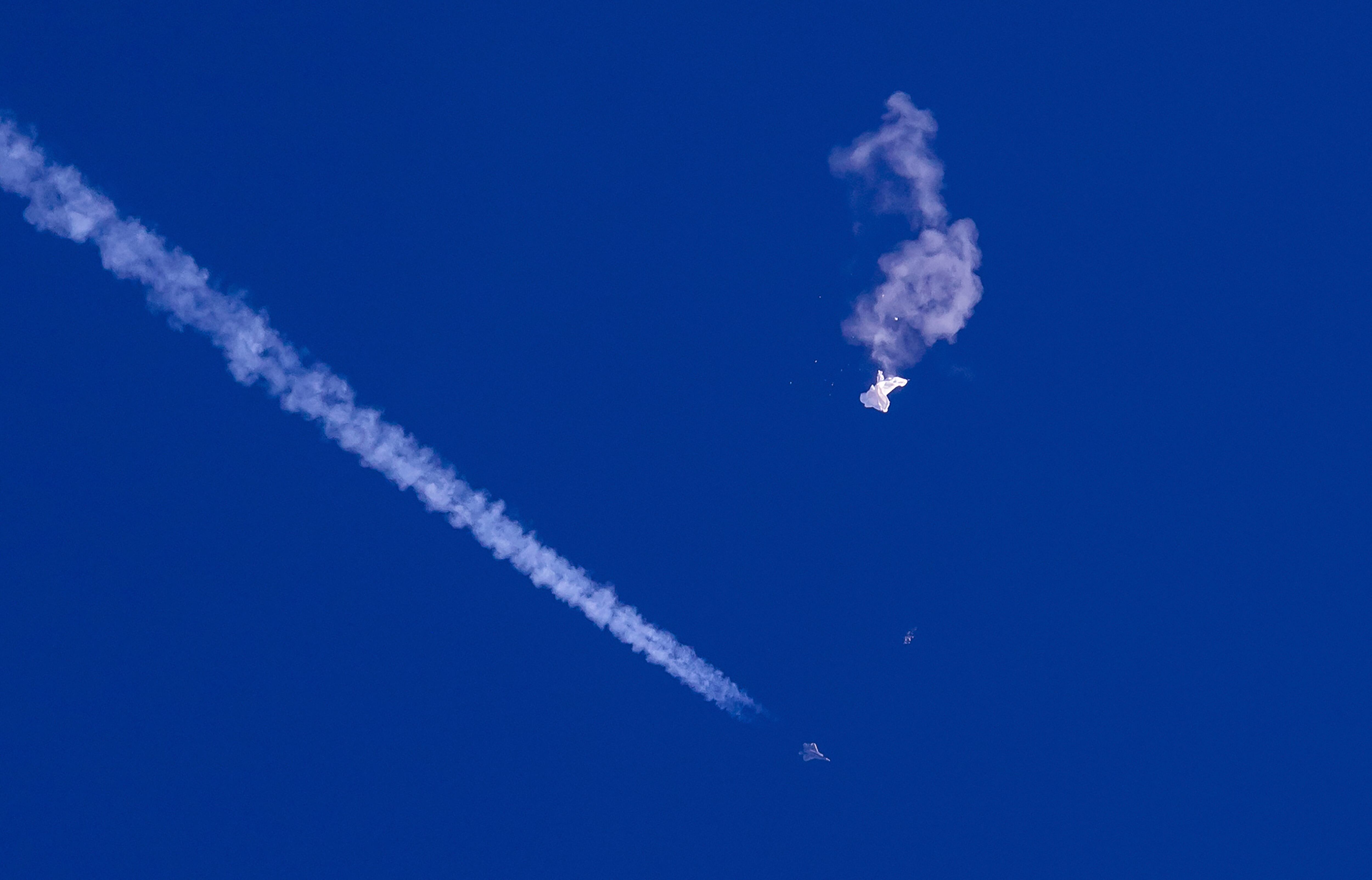 In this photo provided by Chad Fish, the remnants of a large balloon drift above the Atlantic Ocean, just off the coast of South Carolina, with a fighter jet and its contrail seen below it, Feb. 4, 2023.