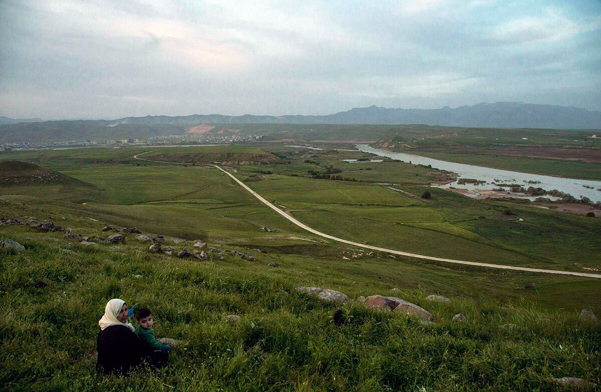 In this file photo dated May 1, 2019, a woman and child sit on a hill overlooking the Euphrates River as families picnic on May Day, in Derik, Syria.