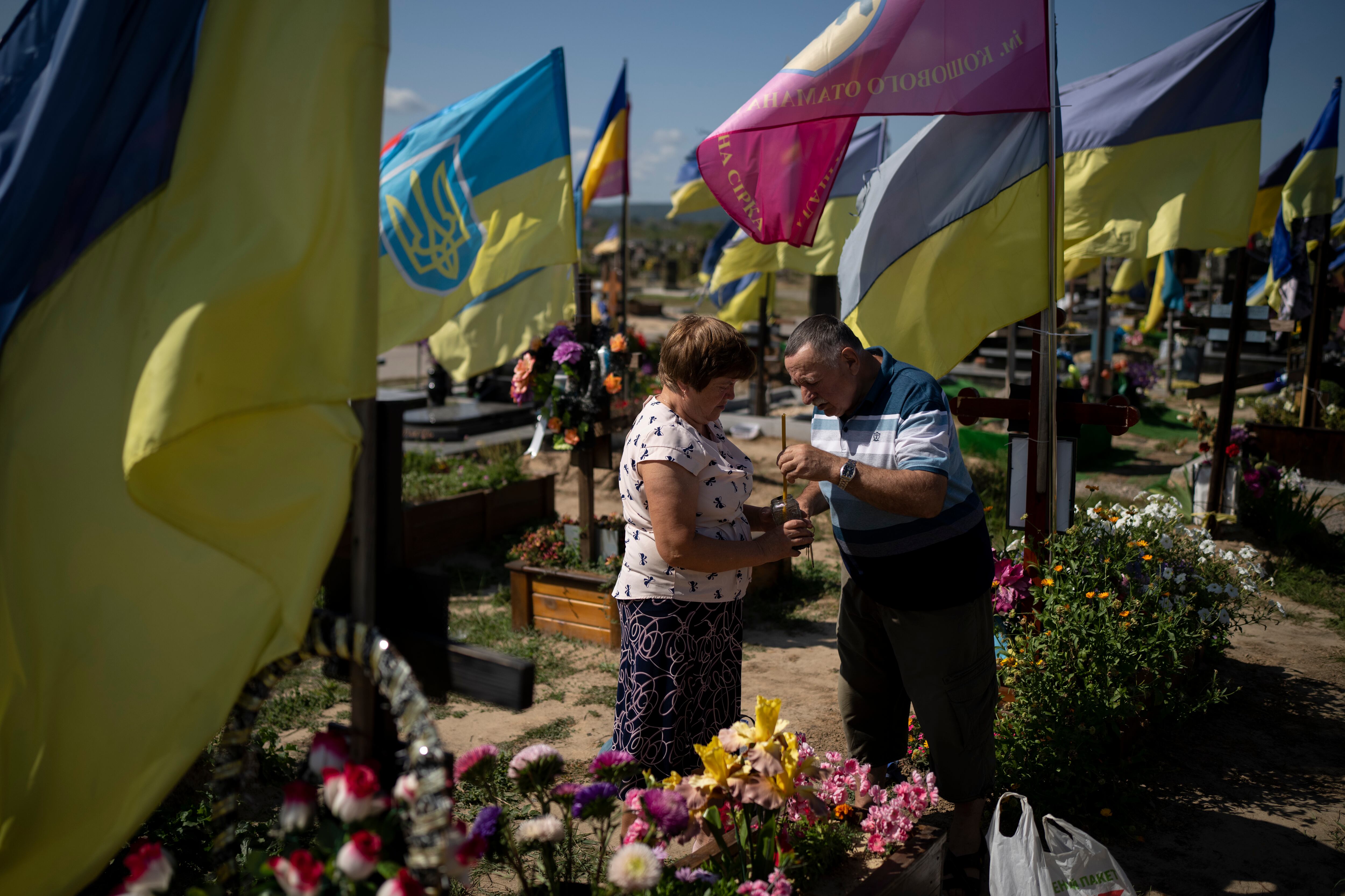 Kateryna and Oleh light a candle at a cemetery in front of their son's grave, who died fighting in the war as Ukrainians mark Independence Day in Kharkiv, Ukraine, Thursday, Aug. 24, 2023.